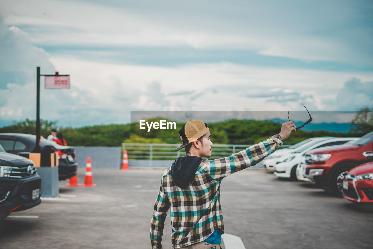 Rear view of man holding sunglasses while standing on road against sky