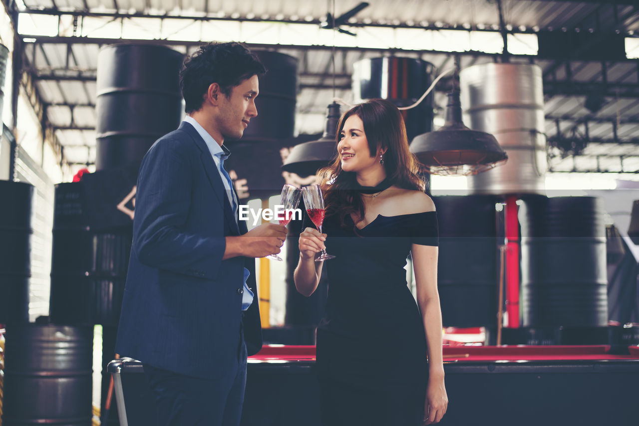 Smiling couple toasting red wineglasses while standing in bar