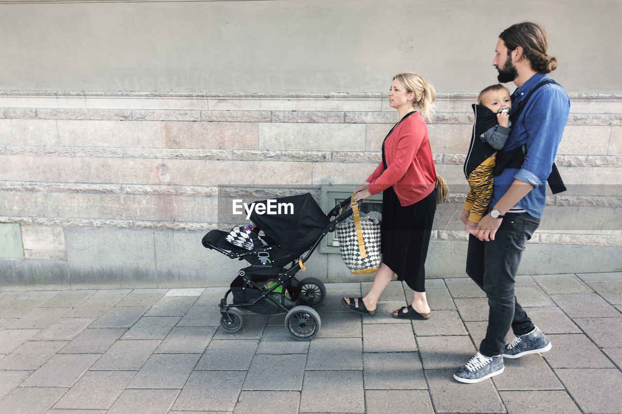 Full length of mid adult parents with baby boy and carriage walking on sidewalk