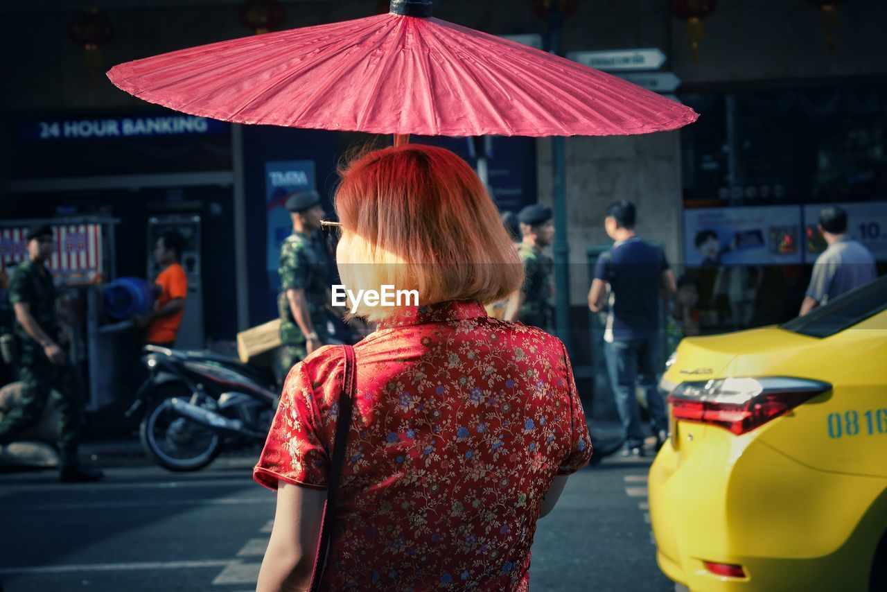 Rear view of woman holding umbrella while walking on street in city