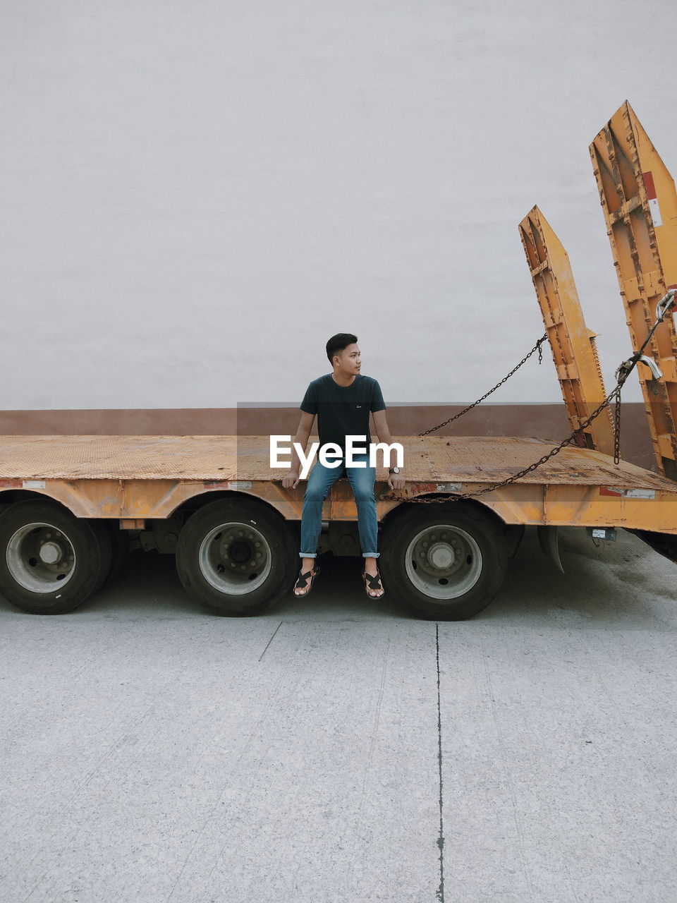 Young man looking away while sitting on truck against sky