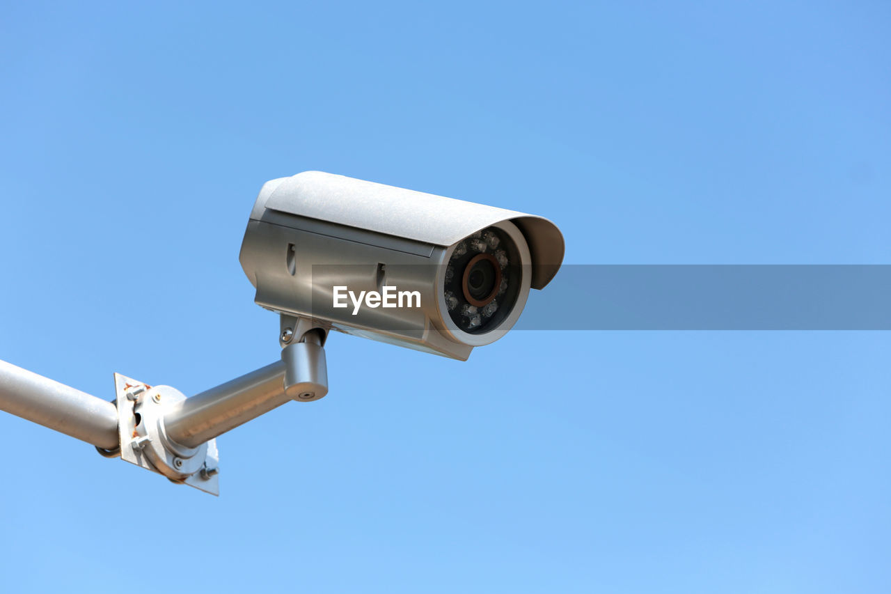 Low angle view of security camera against clear blue sky