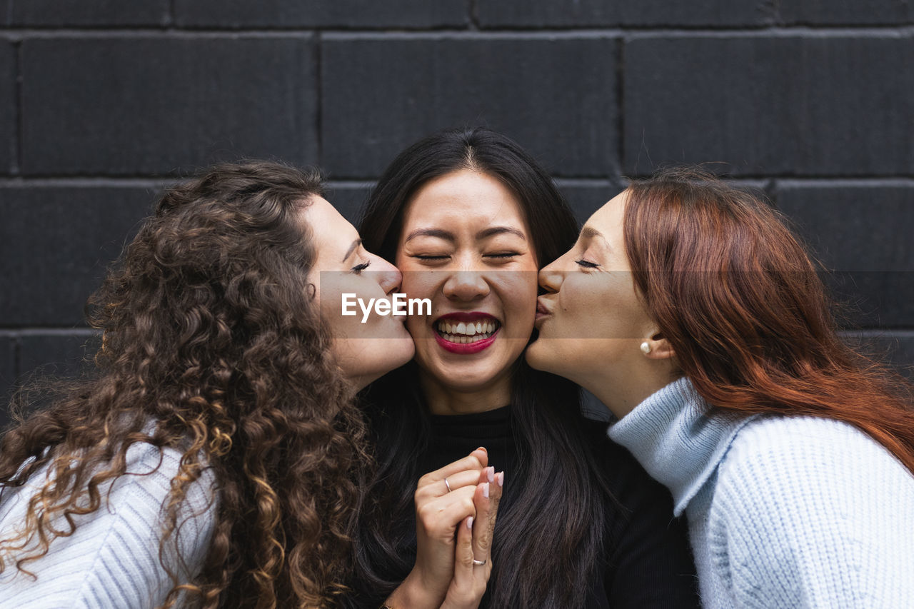 Young female friends kissing happy woman