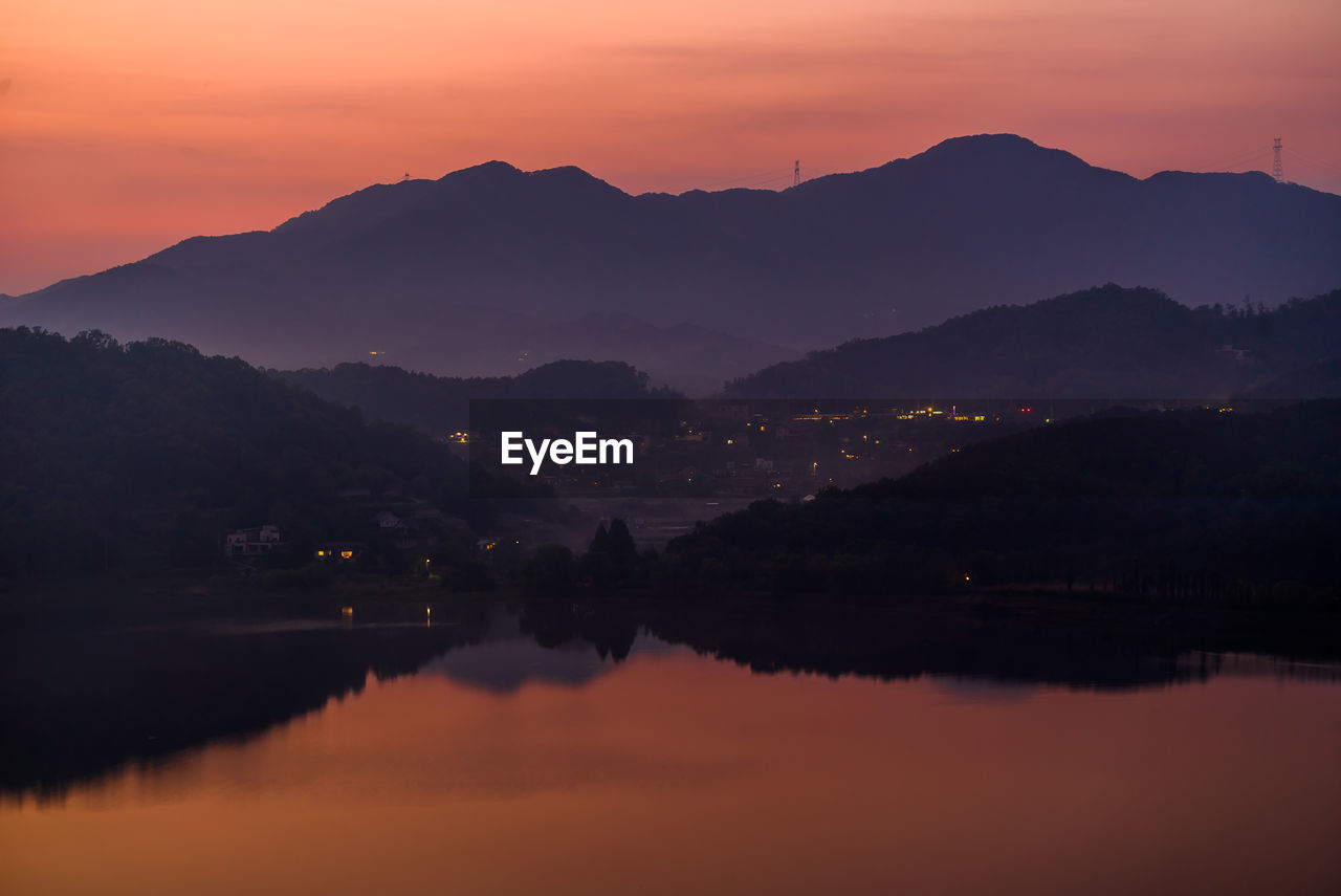 Scenic view of lake by silhouette mountains against orange sky