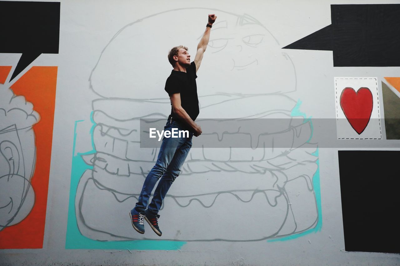 Side view of young man with hand raised jumping against wall