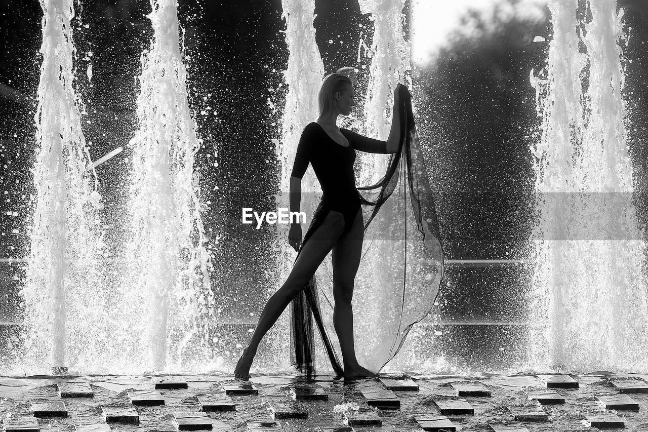 water, one person, black and white, motion, fountain, lifestyles, splashing, monochrome, monochrome photography, women, adult, nature, waterfall, full length, leisure activity, black, water feature, wet, day, standing, young adult, enjoyment, sports, outdoors, swimming, person, female, clothing