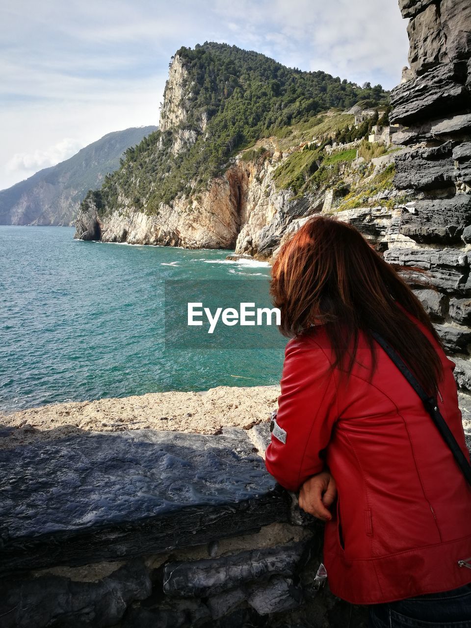 REAR VIEW OF WOMAN STANDING ON ROCK BY SEA