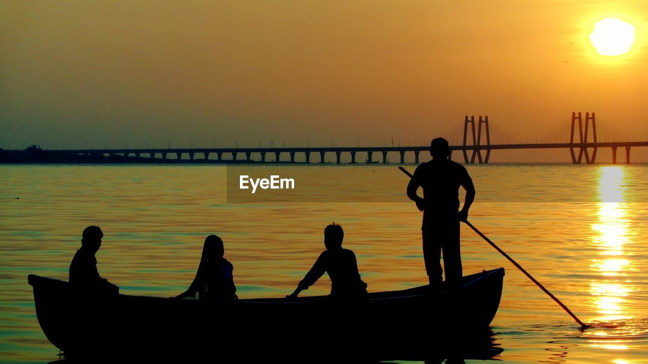 Silhouette people on boat in sea against sky during sunset