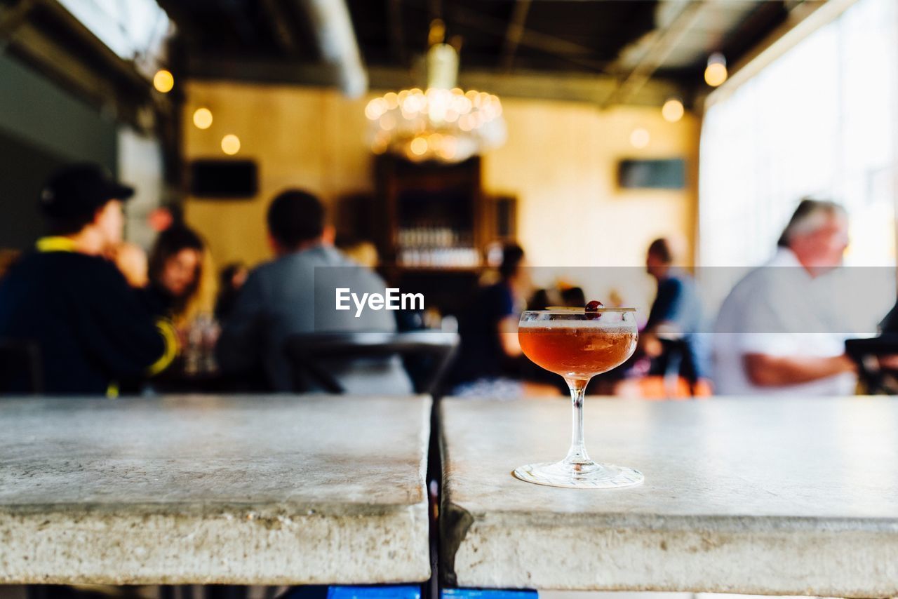 Glass of cocktail on table against people sitting at restaurant