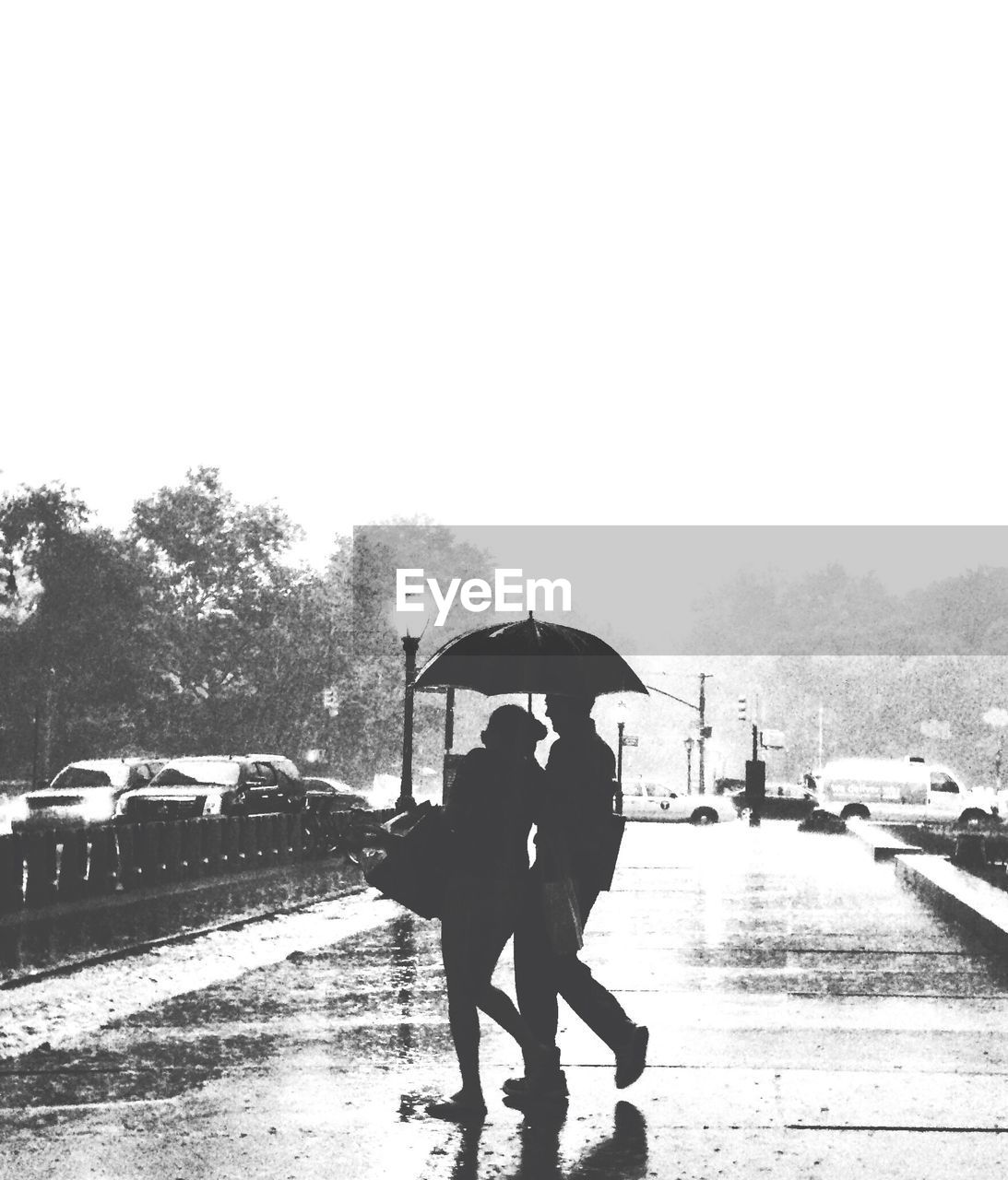 Silhouette couple holding umbrella and walking on wet street during monsoon