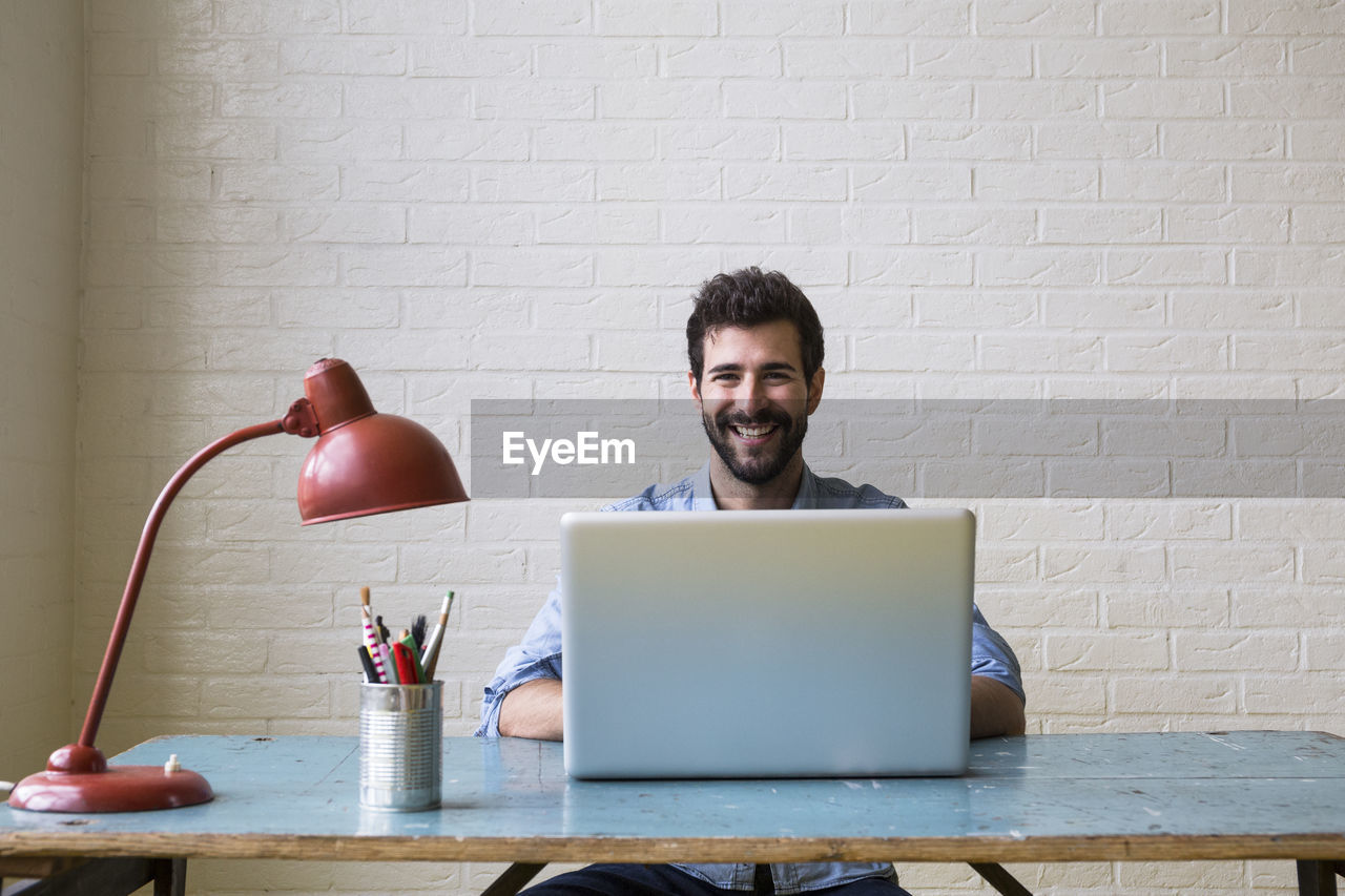 Portrait of happy young man sitting at desk working with laptop