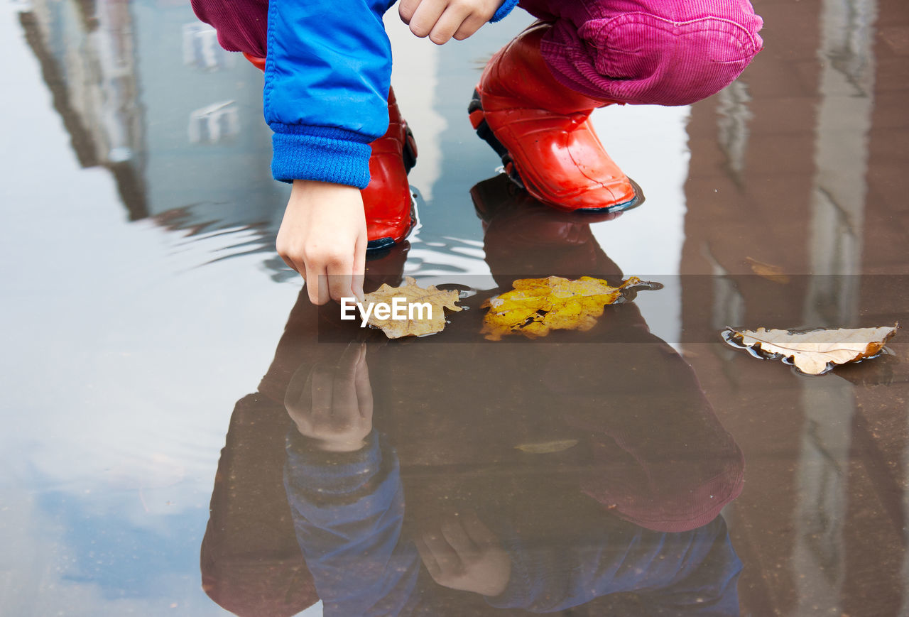 Low section of girl wearing rubber boots while picking leaf from puddle
