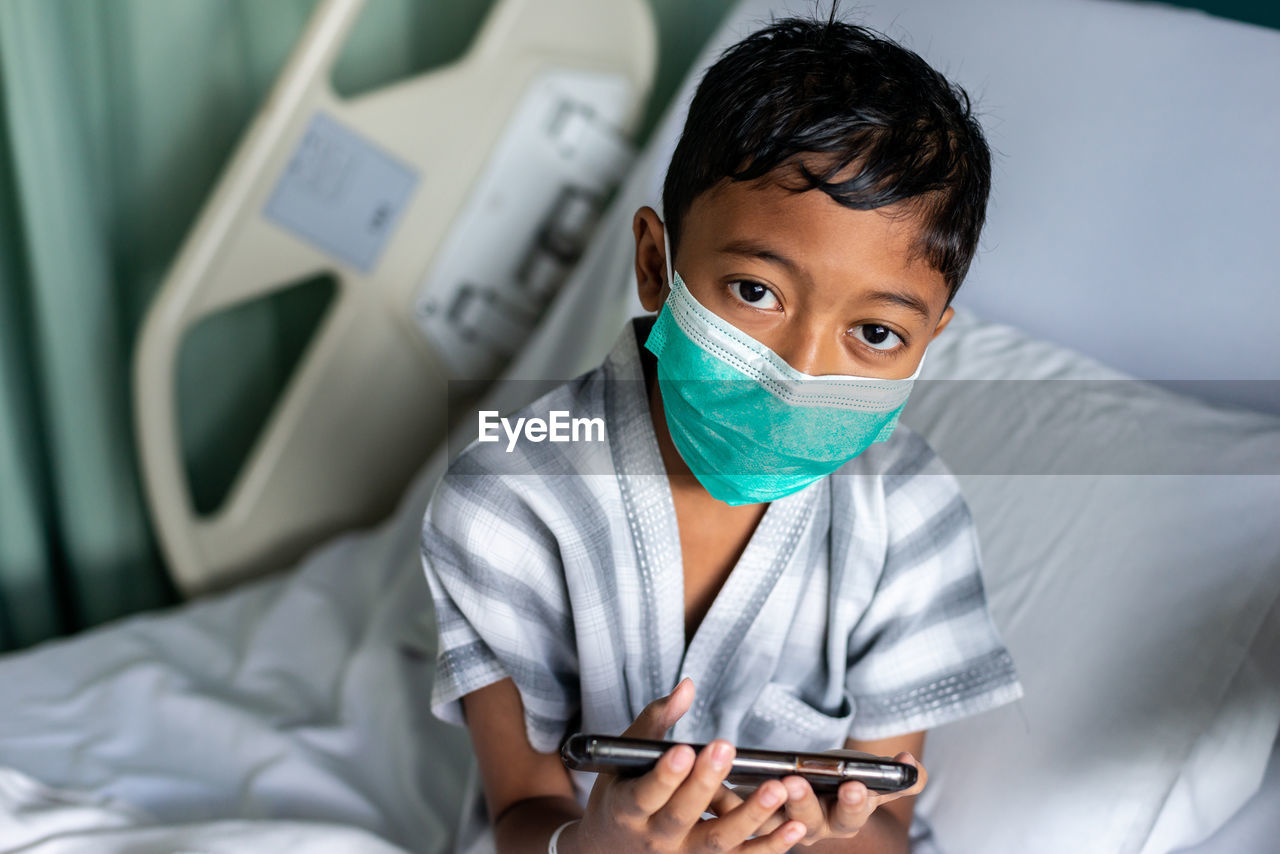 Young muslim boy wearing a mask playing on his smartphone. covid-19 coronavirus concept.