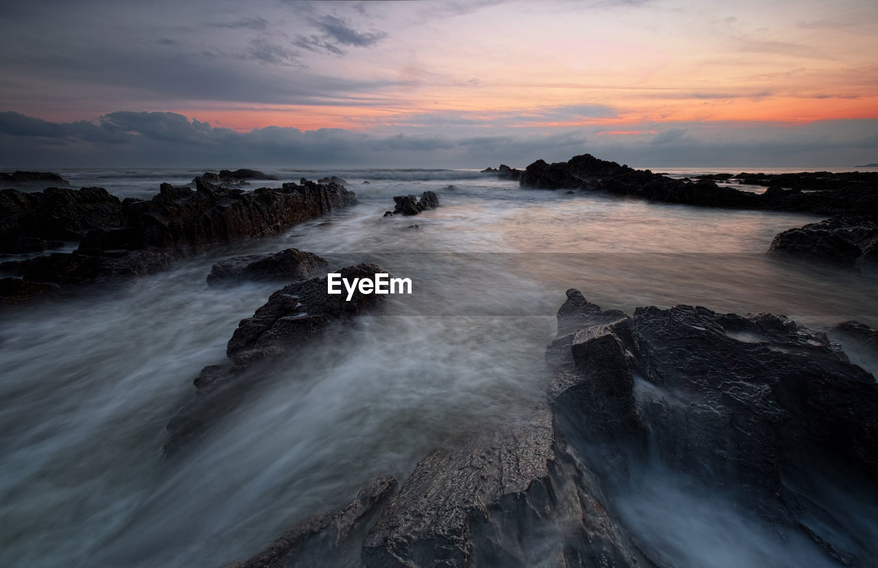 Rocks in sea against sky during sunset