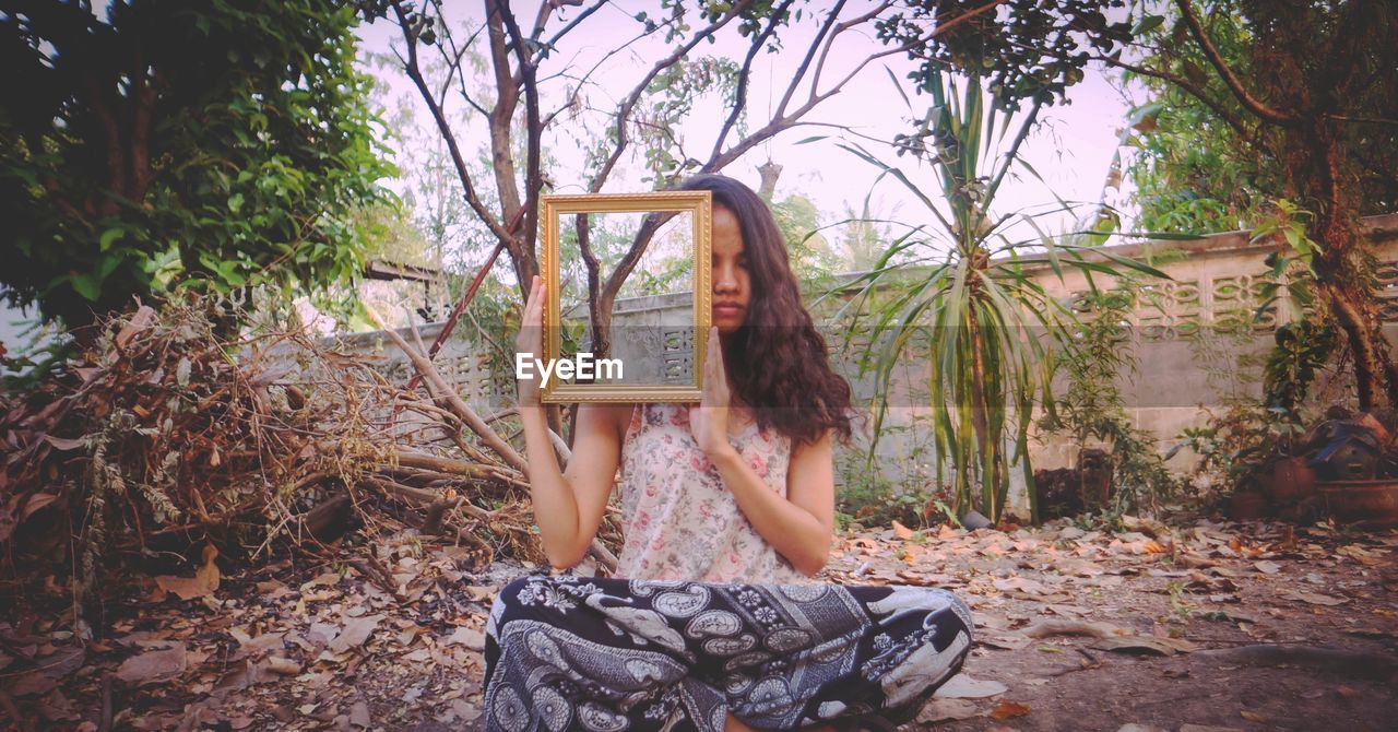 Woman holding picture frame while sitting in messy backyard