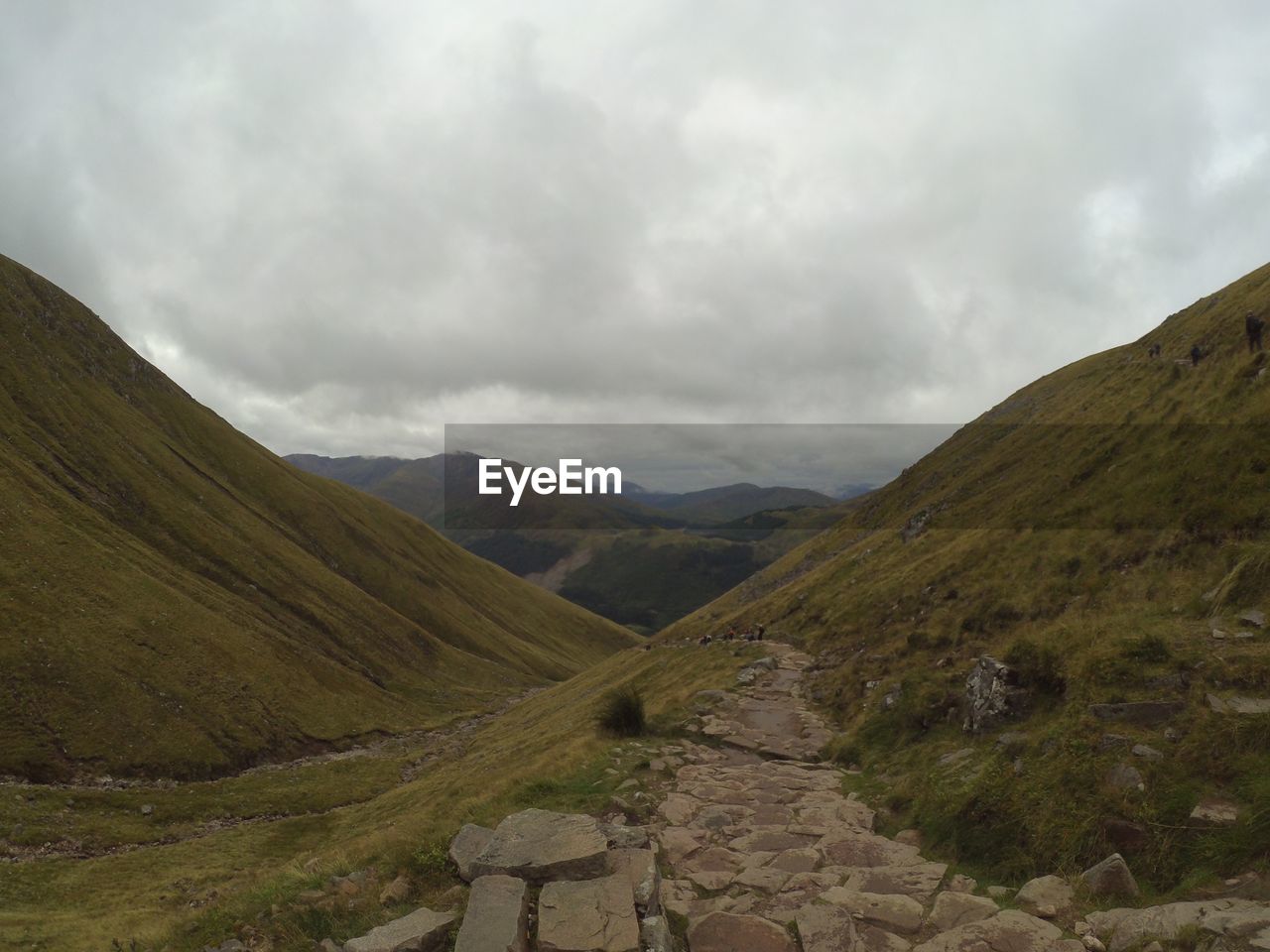 Scenic view of path in valley against cloudy sky