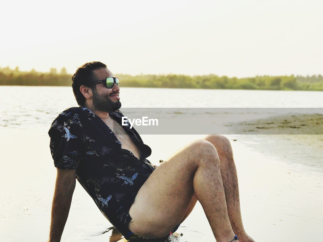 Smiling man relaxing at beach against sky