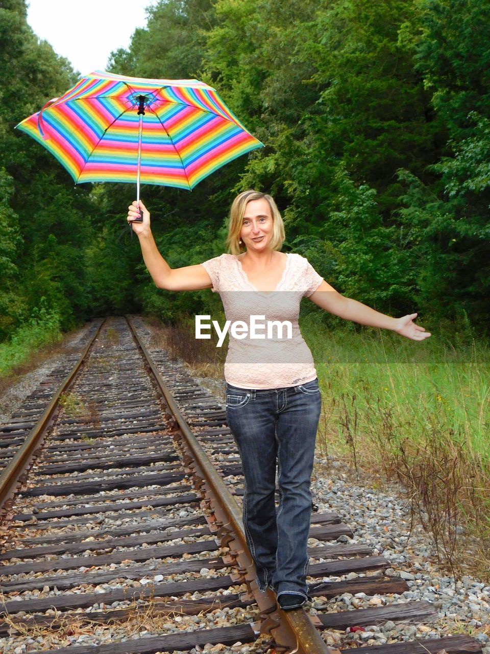 Full length portrait of woman with umbrella walking on railroad track