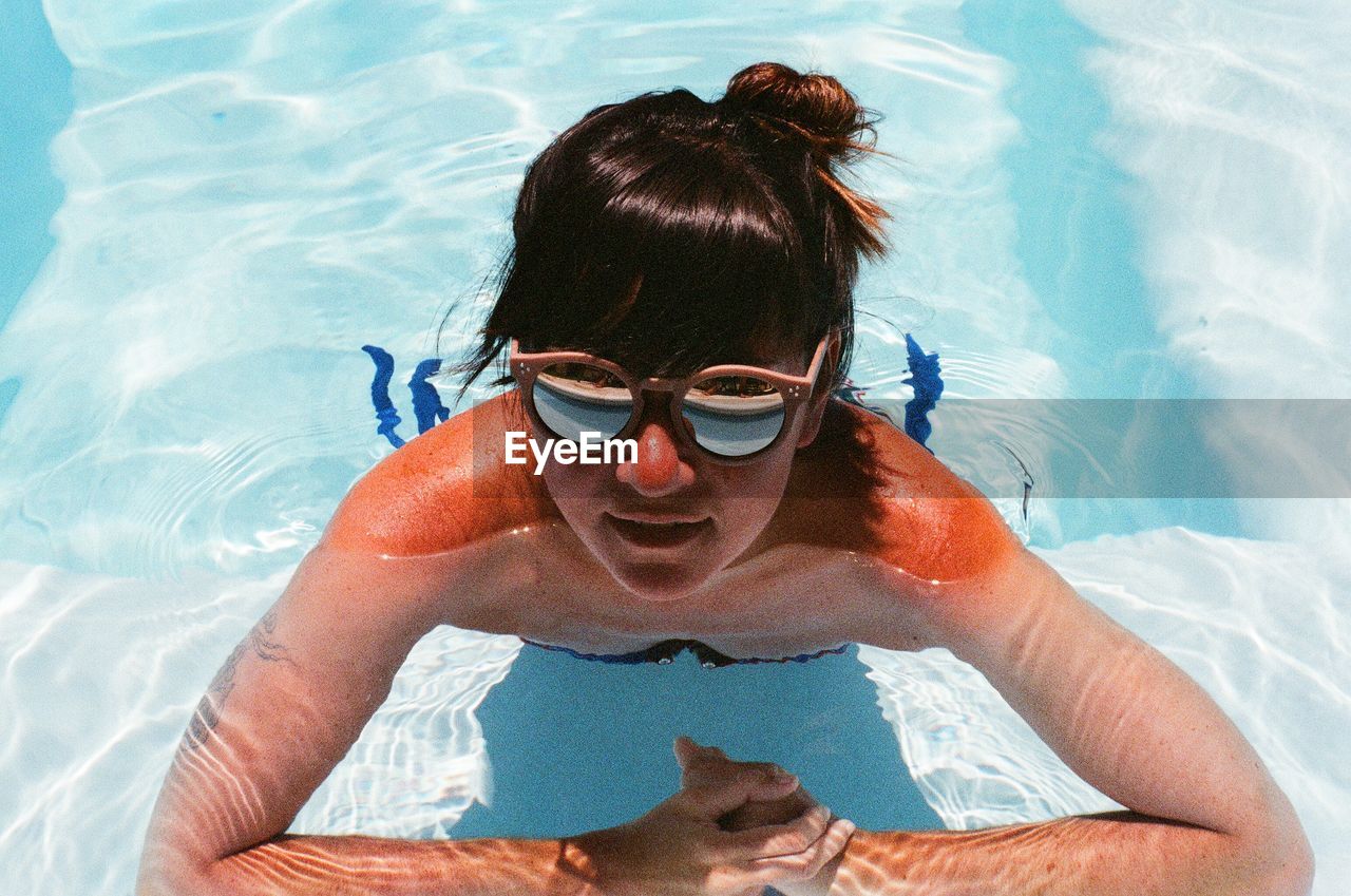 High angle view of woman with sunglasses in swimming pool during sunny day