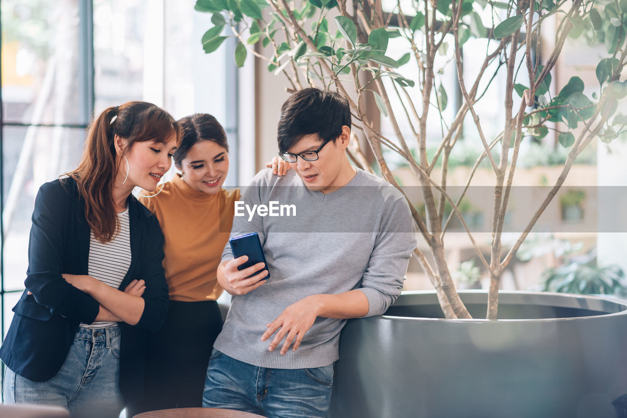 Business people looking at smart phone while standing in office