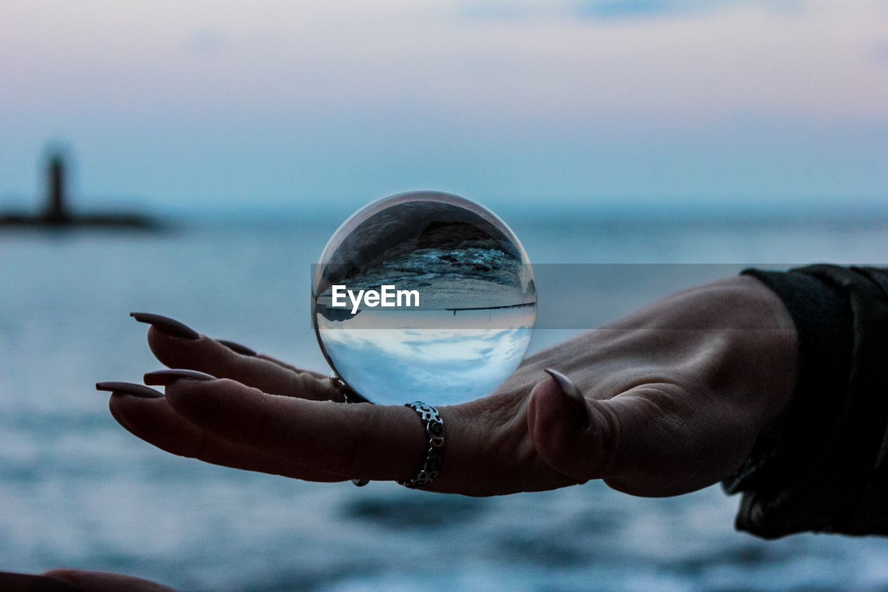 Close-up of hand holding crystal ball against sea