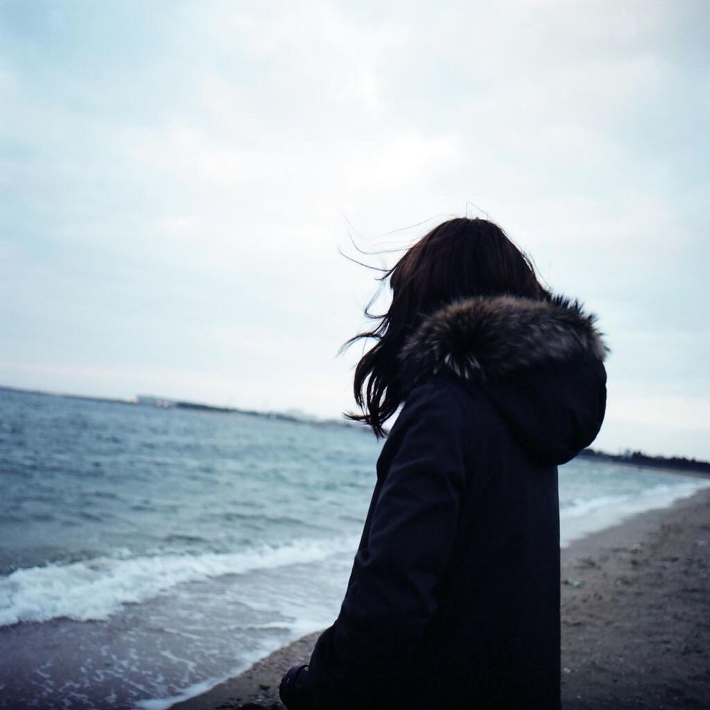 Side view of woman in hooded shirt standing at beach