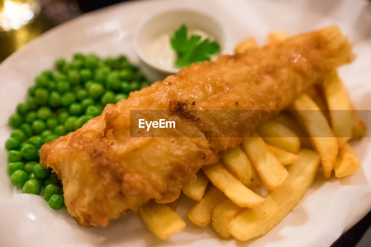 Close-up of fried fish with french fries and peas served in plate