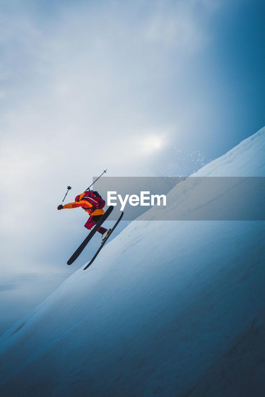 Man flying off ski jump with sun and sky behind him