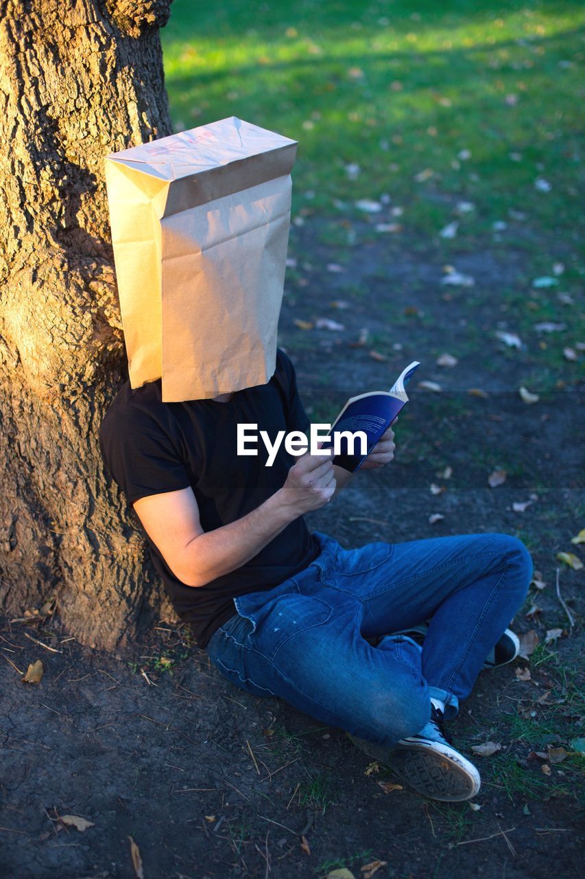 High angle view of man wearing paper bag while reading book outdoors