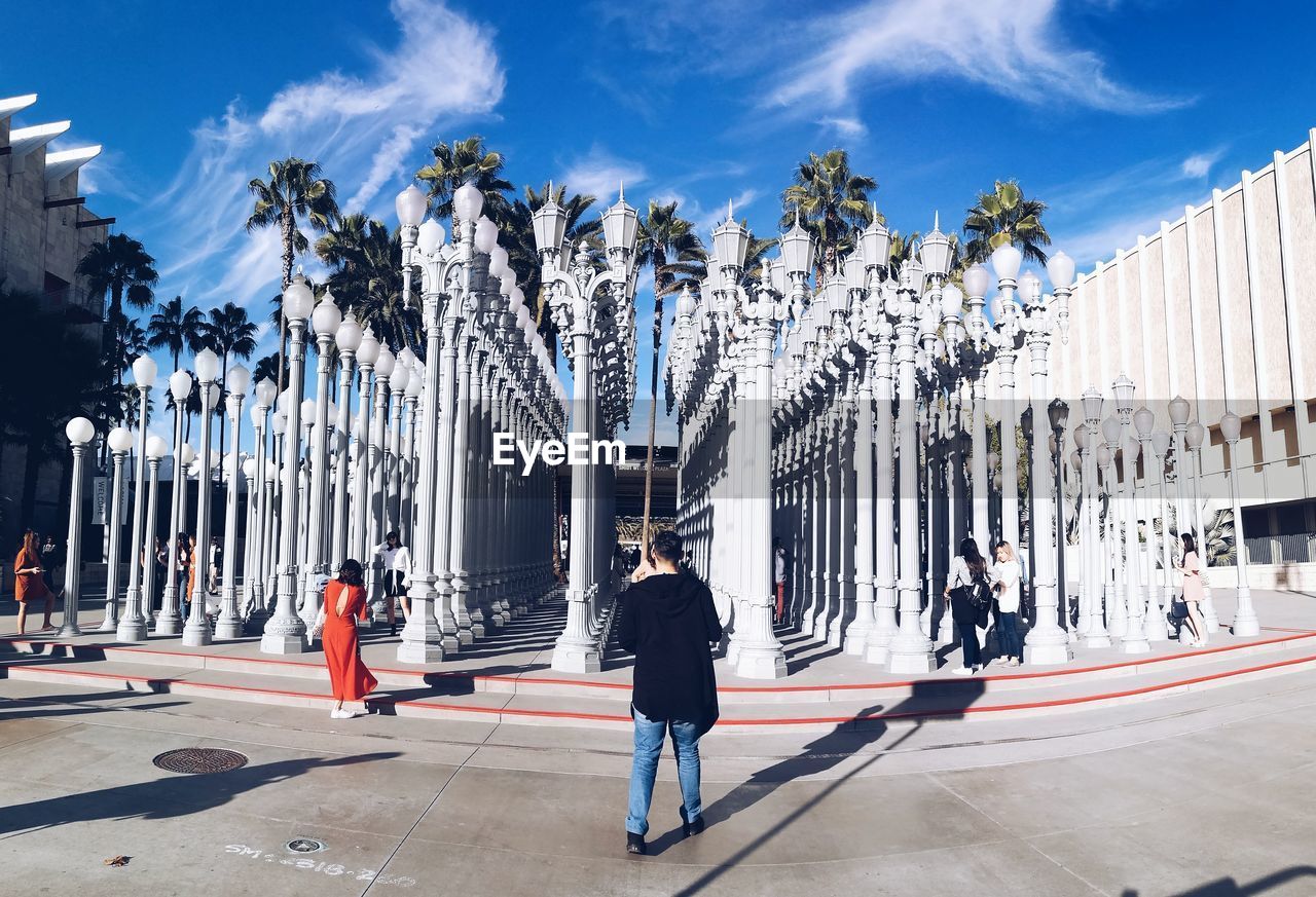 REAR VIEW OF PEOPLE WALKING BY PALM TREES