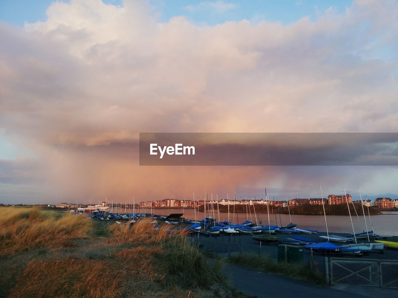 Boats moored at riverbank against cloudy sky