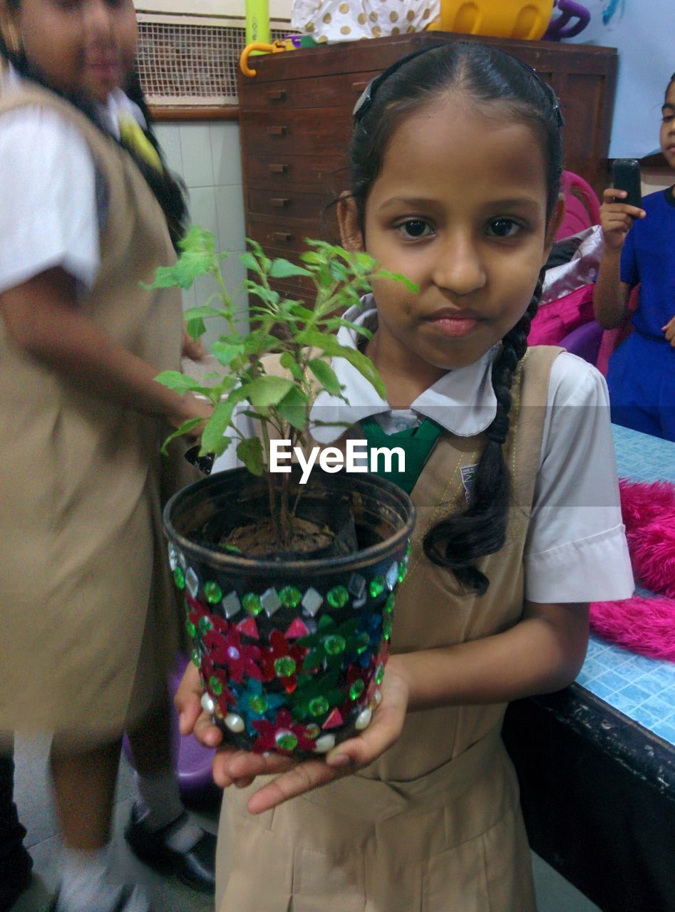 PORTRAIT OF SMILING GIRL HOLDING POTTED PLANTS