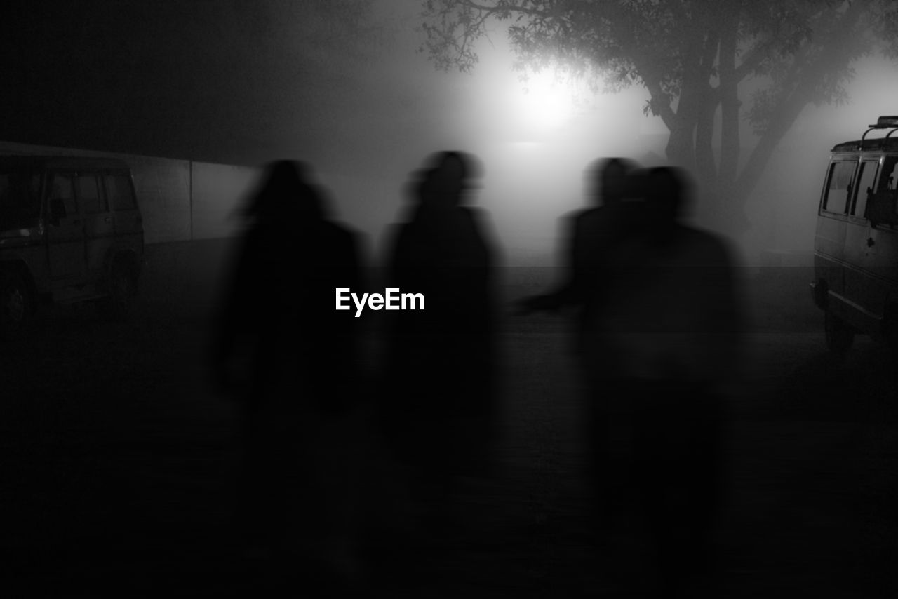 Silhouette people standing outdoors in foggy weather at night