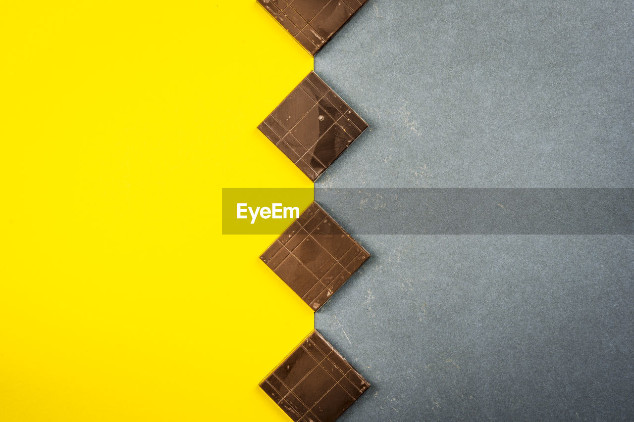 Chocolate bars create geometric shapes on a yellow and gray background. top view