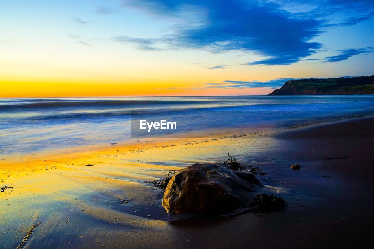 SCENIC VIEW OF BEACH AGAINST SKY AT SUNSET