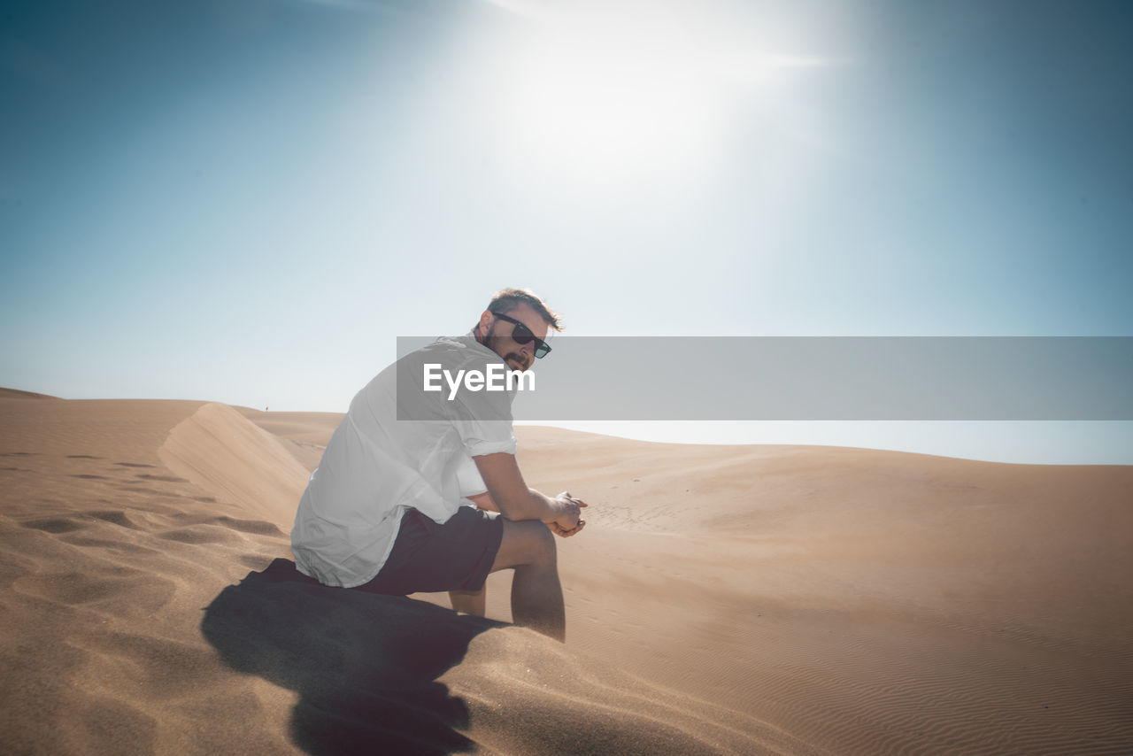 Portrait of man sitting on sand at desert against sky