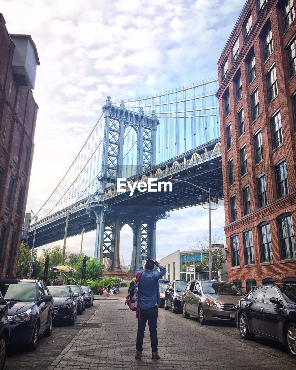 Rear view of man standing against manhattan bridge in city