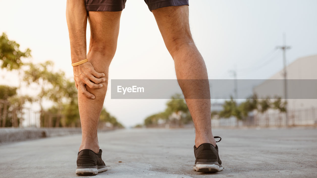 LOW SECTION OF MAN STANDING BY FOOTPATH IN CITY