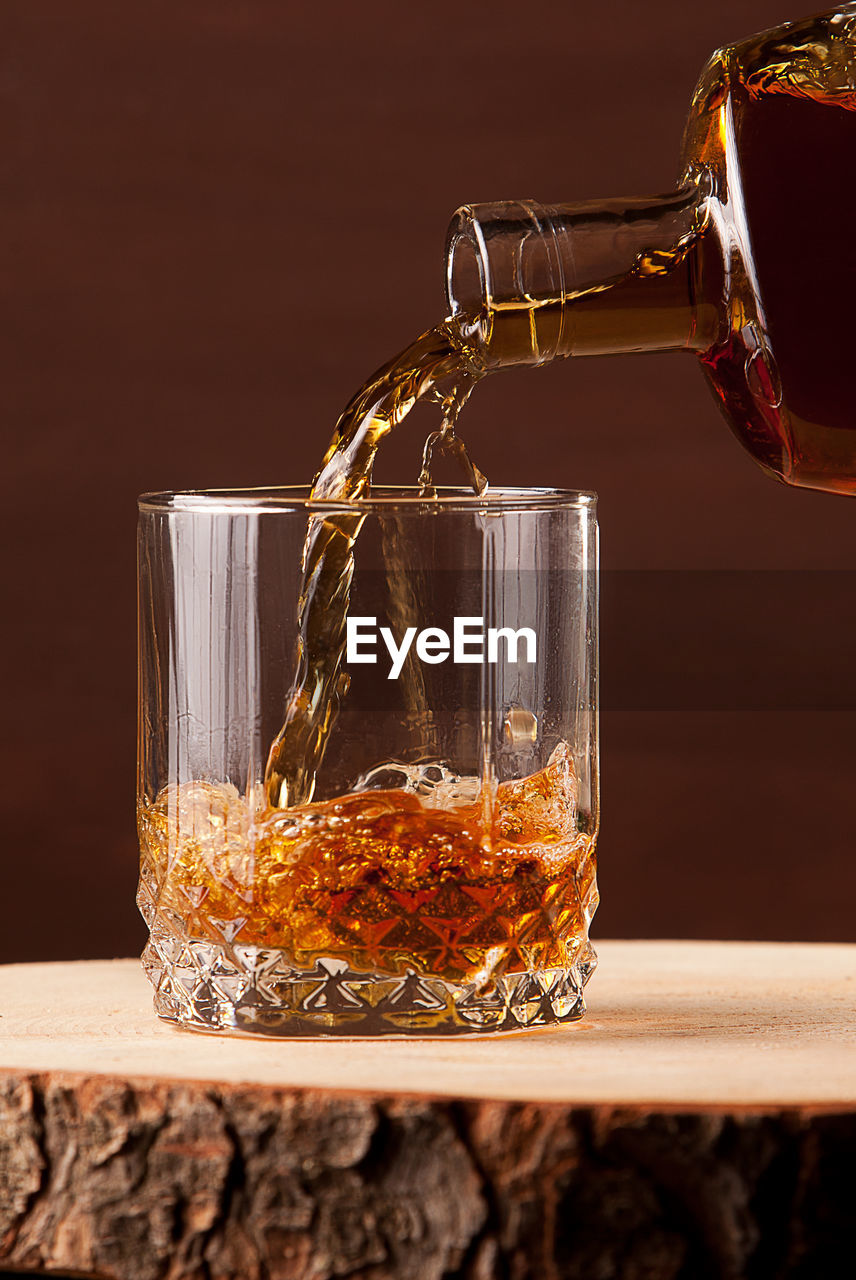 Whiskey glass on wooden table, brown background