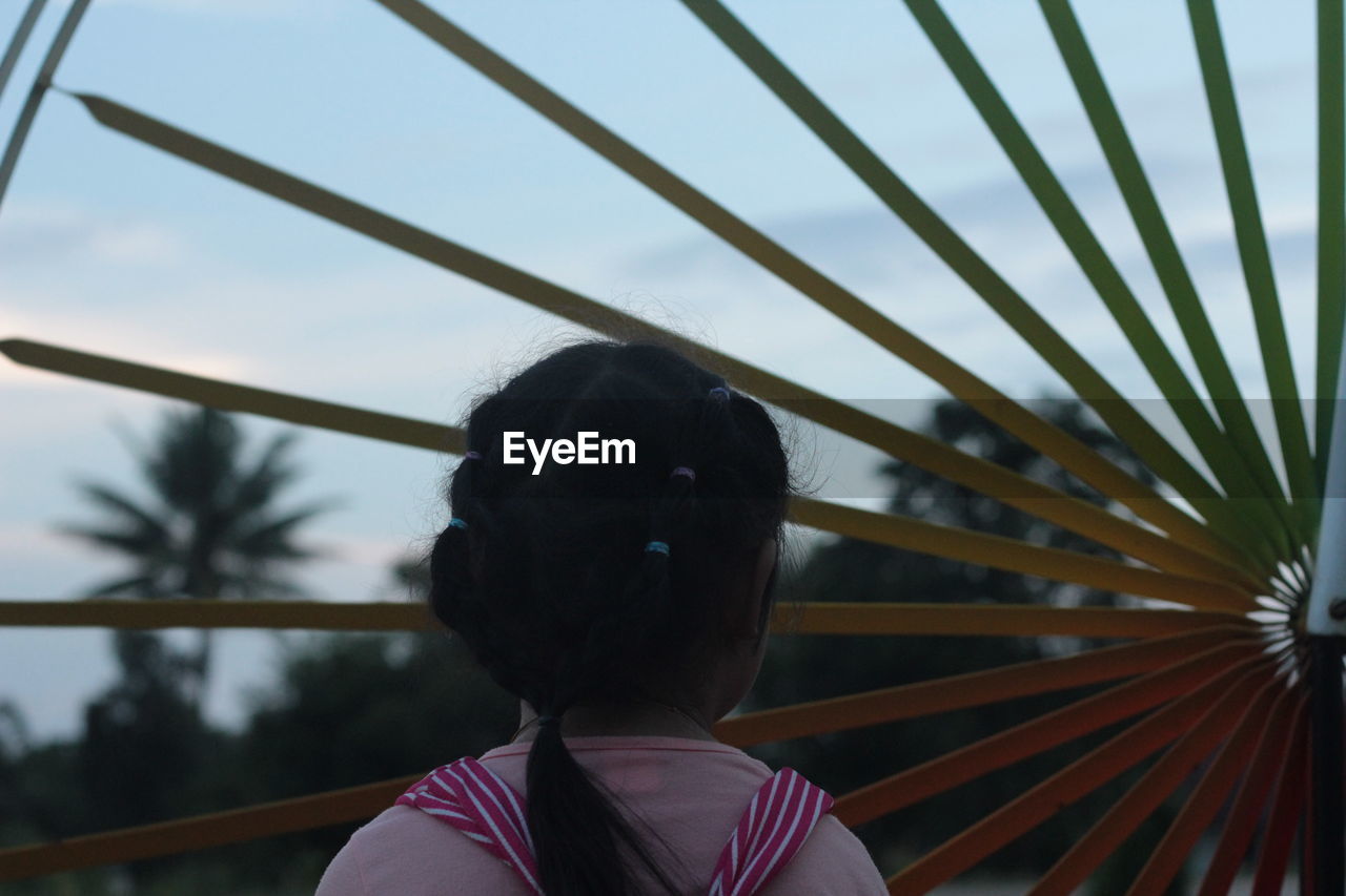 Rear view of girl standing by wheel against sky during sunset