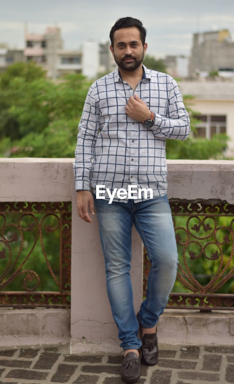 Portrait of young man standing against railing