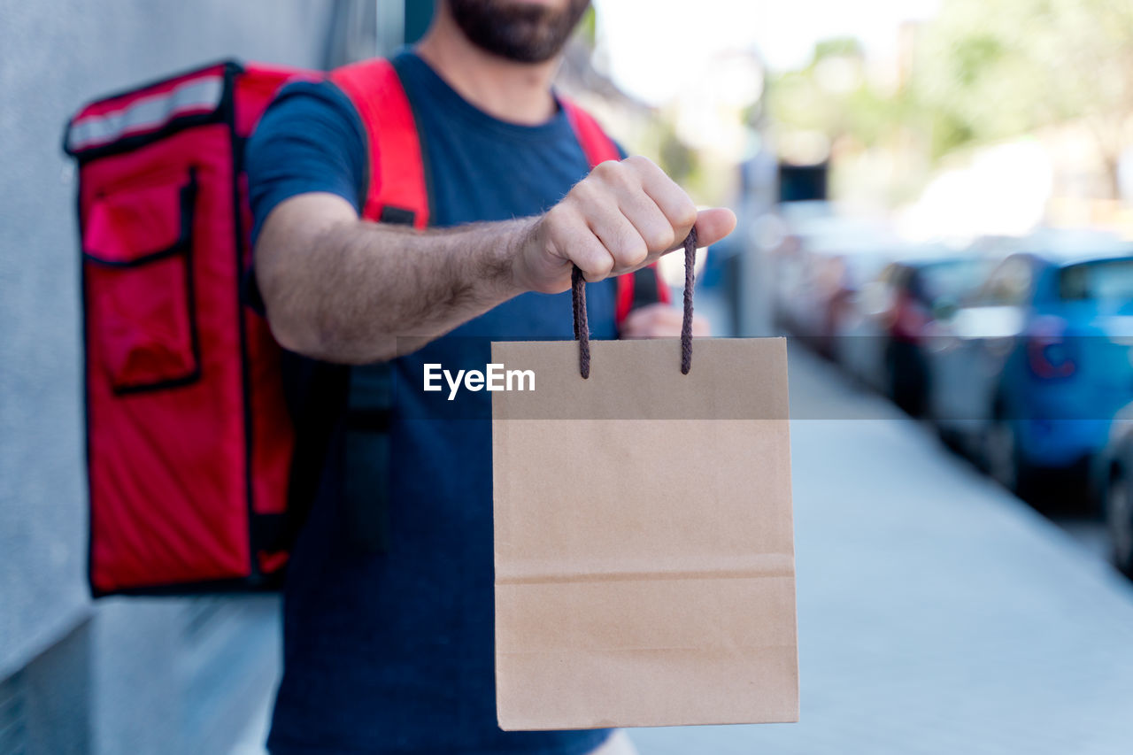 Midsection of delivery person holding cardboard bag