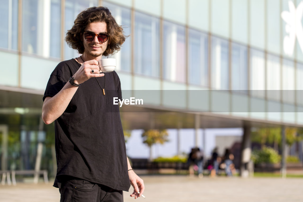 Portrait of smiling young man holding coffee cup and cigarette