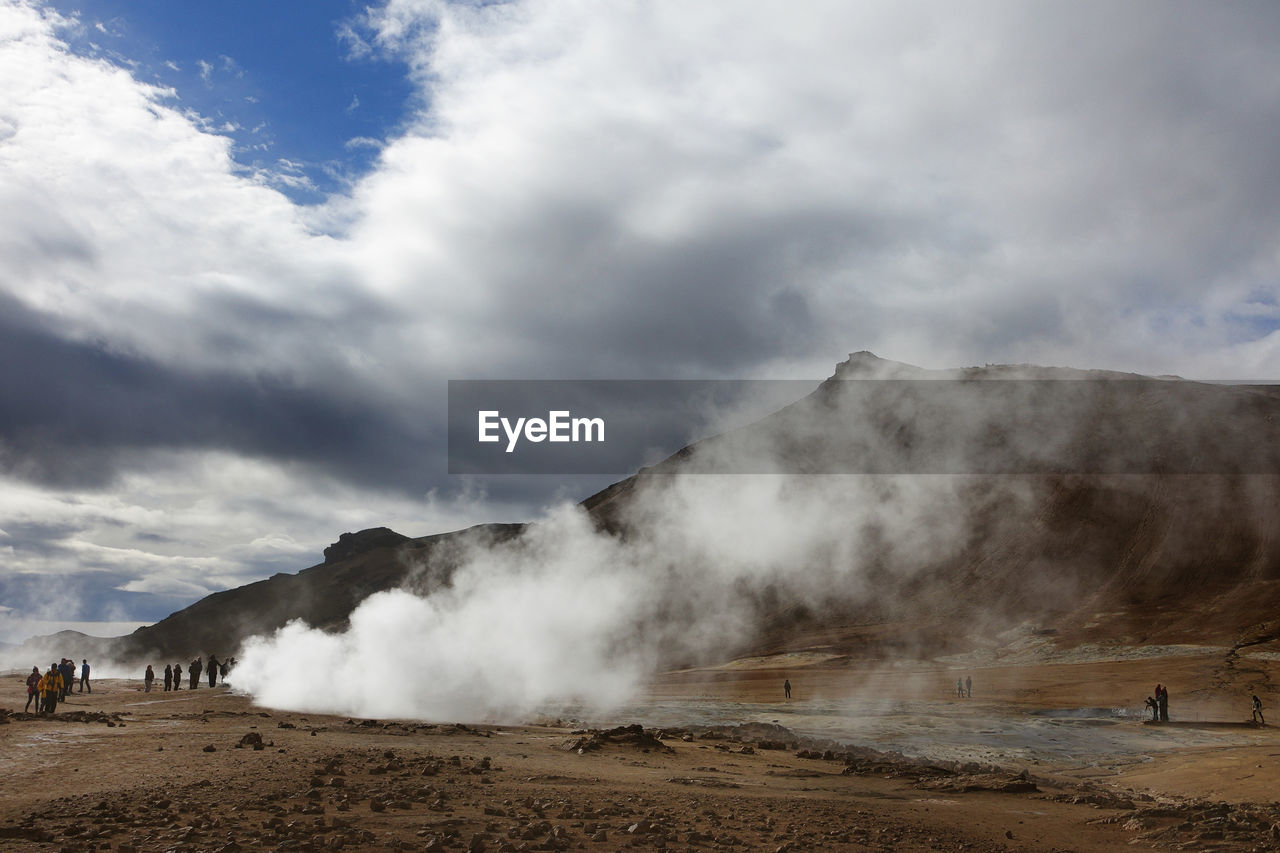 Tourists on landscape against cloudy sky