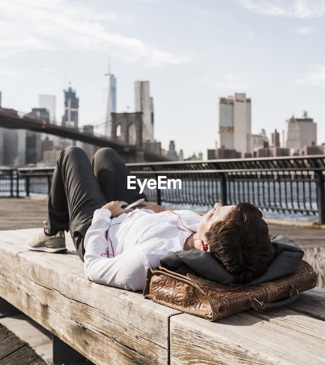 Usa, brooklyn, businesswoman lying on bench listening music with earphones