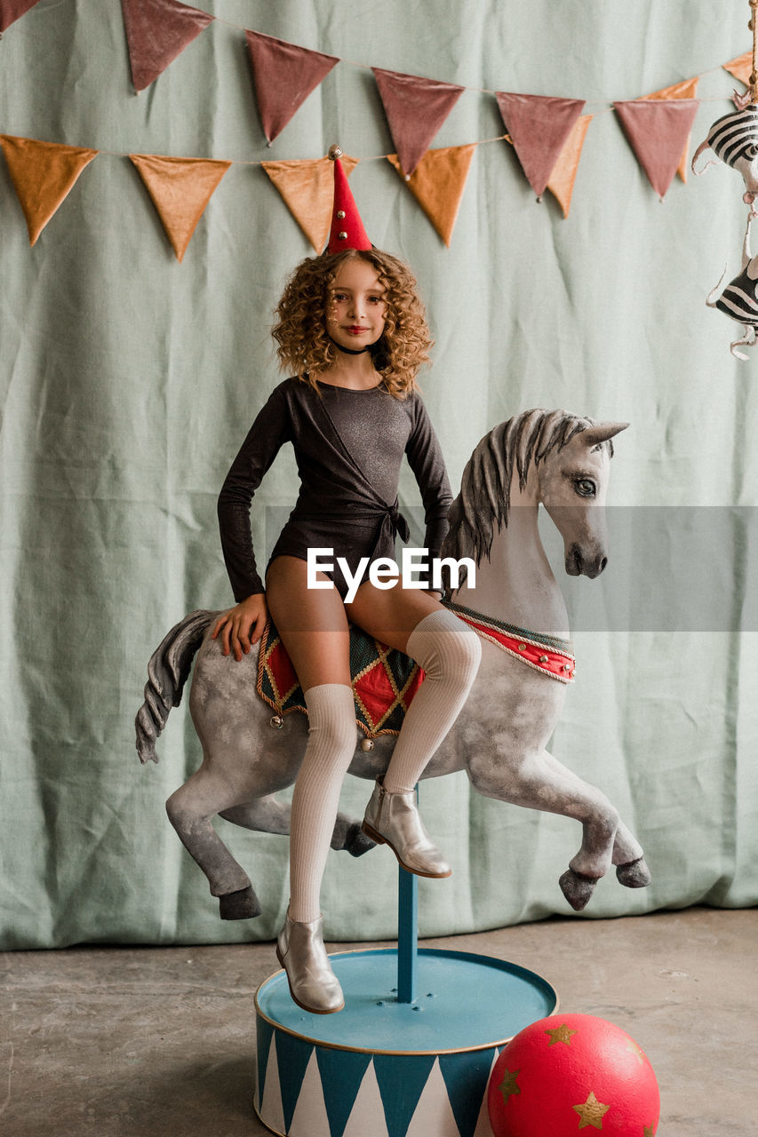 Child girl in circus costume sitting on the carousel horse. halloween