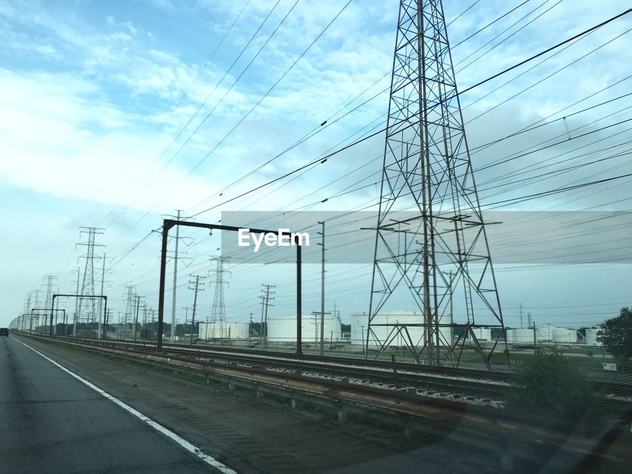 Electricity pylons by railroad tracks against sky