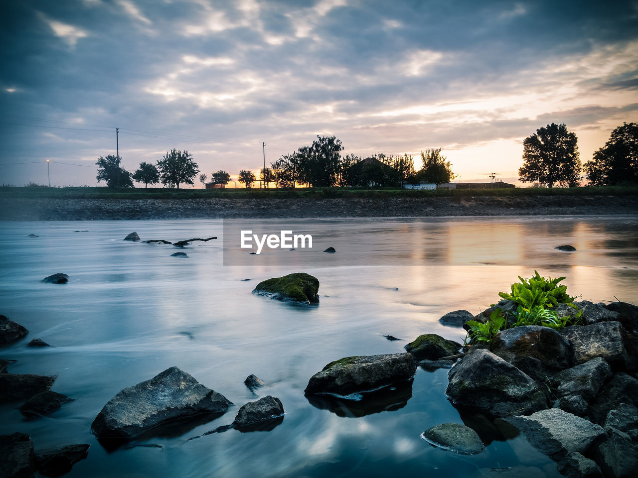 Scenic view of river against cloudy sky at sunrise