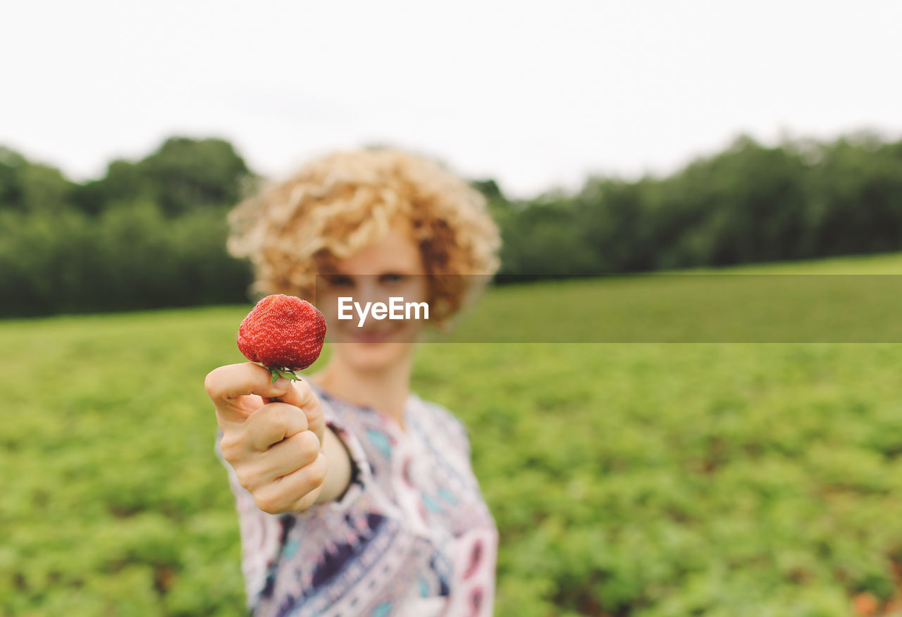 Portrait of smiling young woman showing strawberry on grassy field