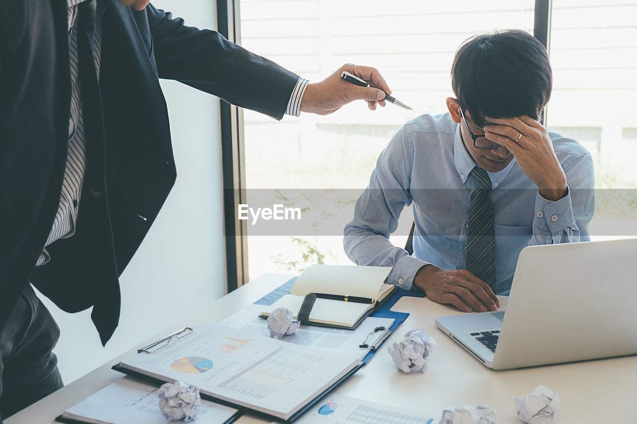 Midsection of businessman scolding stressed colleague at office